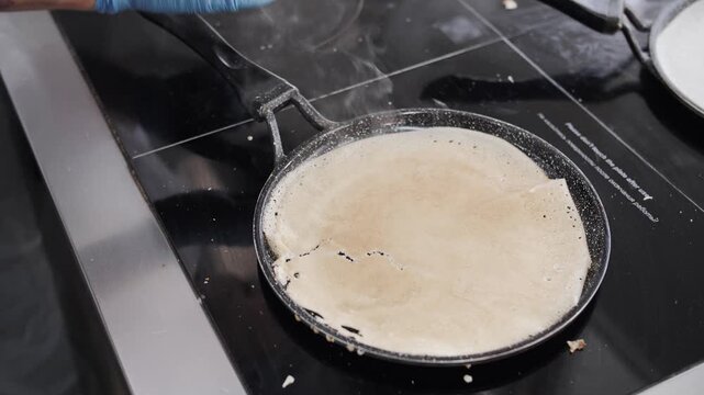 Chef flips a crepe in a hot skillet.