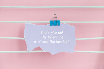 A motivational quote on a pastel pink background. The quote is clipped to a string with a blue clip. The text encourages perseverance and resilience.