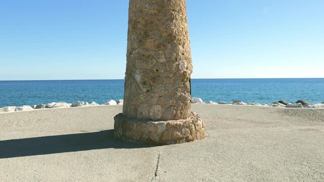 Tilt up view of famous, distinctive, stone-clad lighthouse, locally known as Faro Puerto Ban&uacute;s, Costa del Sol, Marbella, Spain in a clear Mediterranean sunny sky.