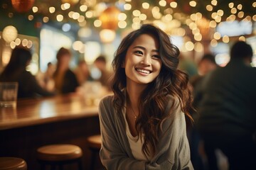 Fototapeta premium A woman sits at a bar and smiles while friends chat and laugh around her. The place is bright with many lights hanging above, creating a joyful atmosphere for socializing