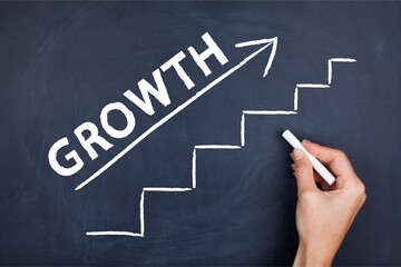 Hand drawing an upward staircase and arrow with the word “GROWTH” on a chalkboard, symbolizing step-by-step progress, personal development, business success, and achievement.
