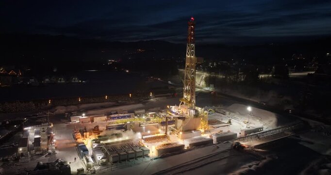 Night drone footage of a geothermal drilling tower. Showcasing industrial processes, heat energy production, and sustainable development in the energy sector.