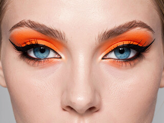 Striking Close-Up of Woman's Eyes with Bold Orange Eyeshadow and Dramatic Black Cat-Eye Makeup