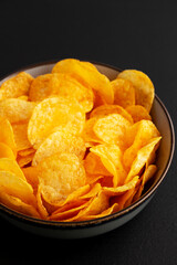Crispy Cheese Potato Chips in a Bowl on a Black Background, side view.