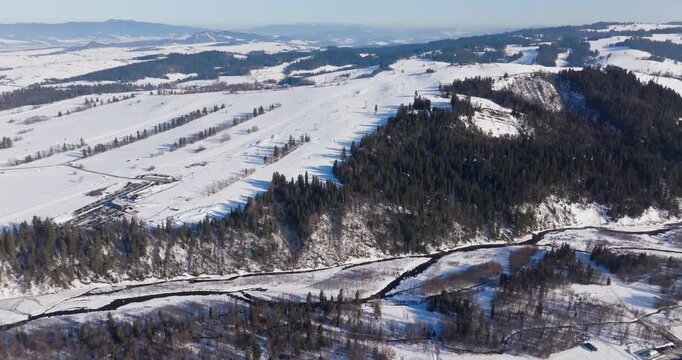 A cinematic drone flyover crossing the Bialka river towards the Grapa Ski slopes on Litwinka hill in Czarna Gora, showcasing winter tourism in Poland.