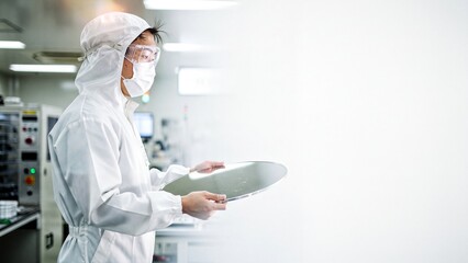 Engineer in cleanroom suit holding a silicon wafer for microchips