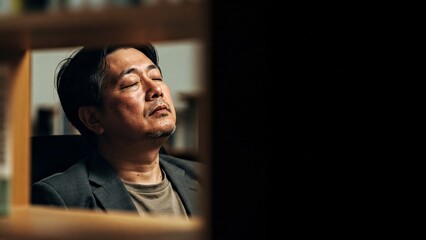 Stressed Asian businessman with eyes closed in a dark office