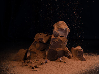 Chocolate pieces with chocolate chips and cocoa sprinkles on dark background