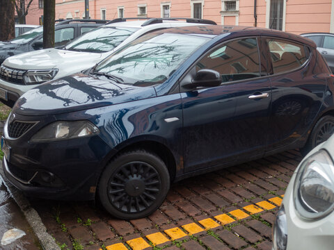 Lancia Ypsilon dark blue hatchback car parked on a European city street with brick pavers and yellow lines
