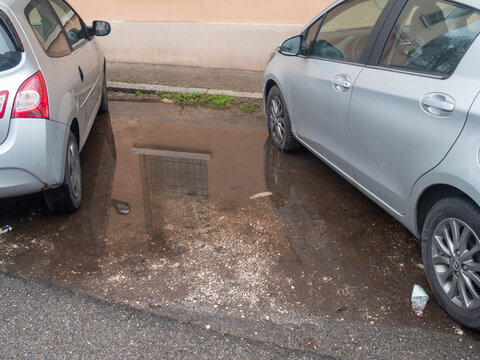 Silver Toyota Yaris and Renault Twingo parked on a street next to a deep rain puddle reflecting a building window