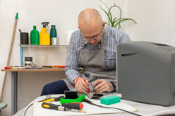 A man with glasses and apron using a multimeter to repair an old television. Electronics repair service for home appliances. Private business concept