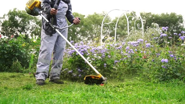 A man with a grass trimmer mows the grass in his yard