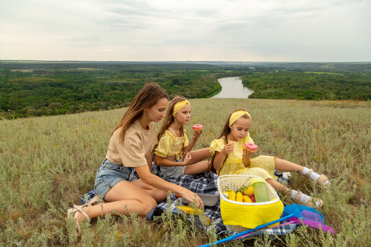 Mom and daughter enjoying picnic in nature, sitting on blanket on grass, eating donuts and having fun together