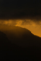 Obraz premium Golden mist above dark mountain slope at sunset Vertical