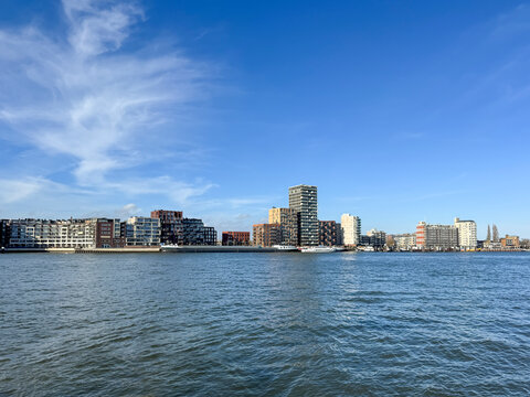 Panoramic landscape view across the river Oude Maas from Dordrecht toward Zwijndrecht skyline featuring modern high-rise apartment blocks, waterfront homes, urban renewal, Dutch riverside architecture