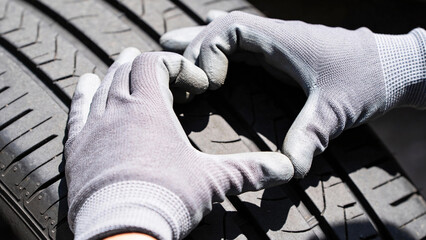 Close-up of gloved hands inspecting tire tread depth on a vehicle tire, showcasing the texture and pattern of the rubber surface in bright outdoor lighting