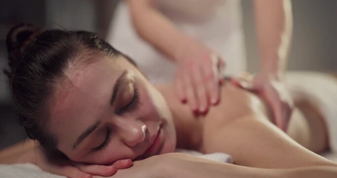 Massage therapy masseuse soothes woman shoulder in spa. Closeup shows client resting as hands ease tension and boost circulation for calming rejuvenation. Concept of wellness, beauty and care.