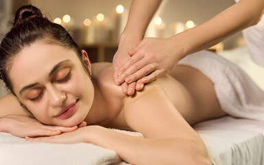 Obraz premium Woman receives massage therapy at spa. Resting client lies as a masseur works the back and shoulders by candlelight, nurturing tranquility and wellness. Calm wellness and relaxation concept.