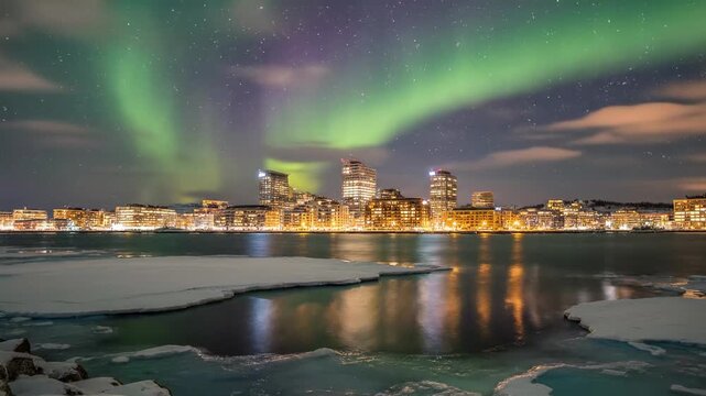A stunning night scene showcases a city skyline illuminated by warm lights, reflecting on icy waters under a vibrant aurora borealis casting colorful hues across the clouds