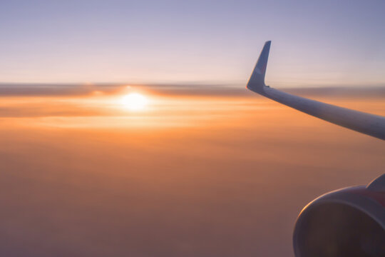 Beautiful background - a plane flying above the clouds and the setting sun on the background, a wing in close-up against the sky. Air travel and tourism, flights and aviation. High quality photo
