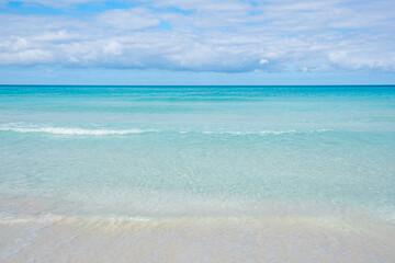 Calm ocean waves gently lap on the sandy shore under a bright blue sky