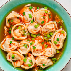 Dumplings served in a bowl with broth and green onions.