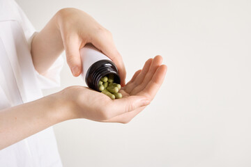 Women's hands pouring green capsules from bottle, representing health supplements and wellness