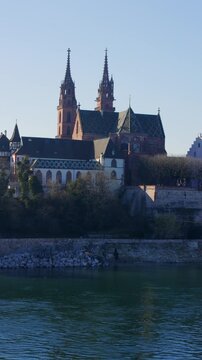 Vertical, static shot capturing the red sandstone towers of the Basel Minster rising behind the modern Wettstein Bridge over the Rhine river in Basel, Switzerland, 4K 10 Bit.