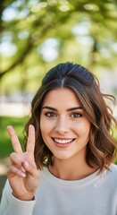 Attractive young woman offers a sign of peace and happiness outdoors with vibrant greenery in background