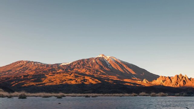 Sunset timelapse of Mount Teide reflected in the waters of Puddle in Ucanca, Teide National Park, Tenerife, Canary Islands. Warm golden light illuminating the volcanic landscape, calm water creatin