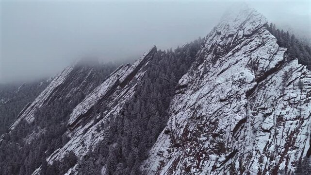 Winter lightly snowing fog Flat Irons rock formations slabs Chautauqua Park trail aerial drone Boulder Colorado sunset dusk evening snowy trees snow falling foggy grey skies low cloud layer forward