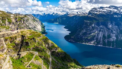 Scenic fjord view with rocky mountains and blue water under cloudy sky, with winding path in the left foreground