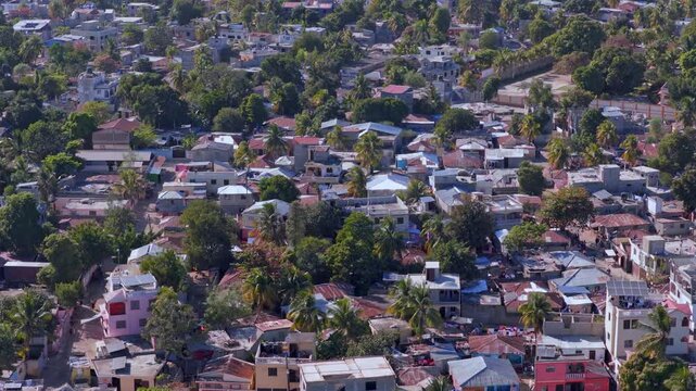 Aerial view of Juana M&eacute;ndez in Haiti showing compact residential housing, mixed rooftops, palm trees, narrow streets and dense urban structure under bright daylight.