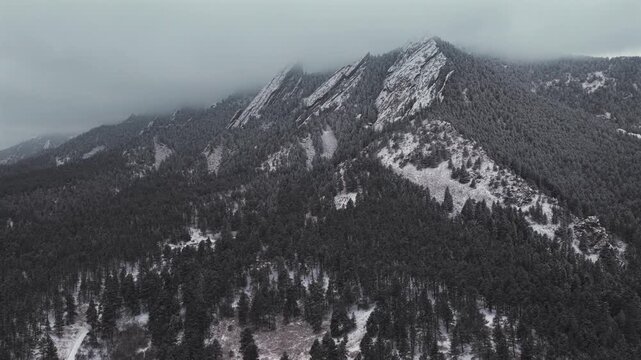 Winter lightly snowing Flat Irons rock formations slabs Chautauqua Park trail Boulder Colorado aerial drone sunset dusk evening snowy trees grey skies foggy low cloud layer snow falling upwards motion