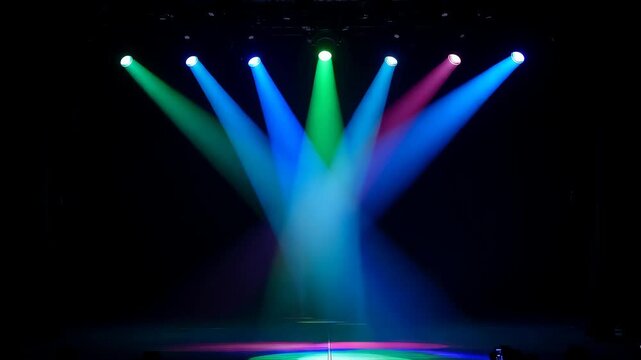 Stage lights with colorful beams shines down in a darkened venue with blue green and red colors