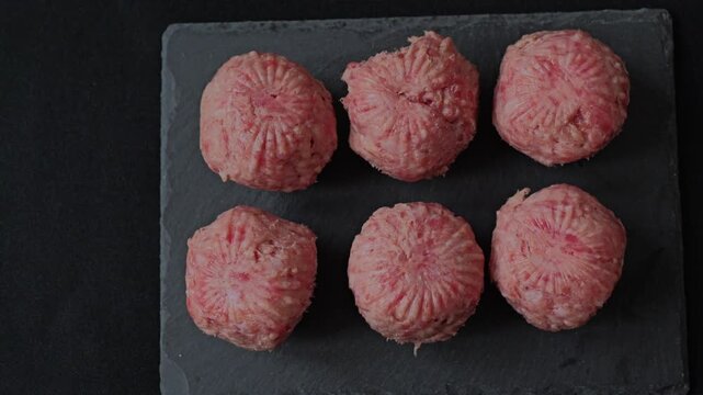 Round meatballs on a dark stone plate in a kitchen setting ready for cooking