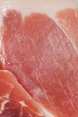 A detailed full frame shot of thin slices of dry cured prosciutto ham showing the marbled texture of meat and fat