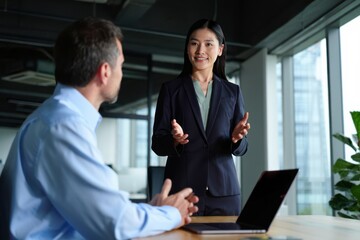 Asian female executive sharing ideas and collaborating with businessman at modern office desk. Businesswoman in teamwork and professional communication in corporate environment.