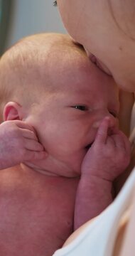 Close-up of tiny newborn baby with eyes closed, finger touching mouth, held by parent