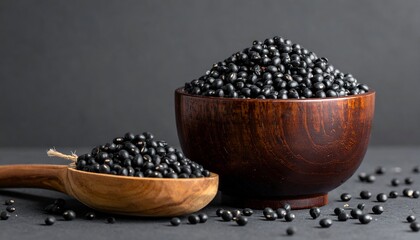 Wooden bowl and spoon overflowing with dried black beans, set against a dark gray backdrop, close-up food still life