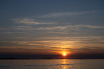 Fototapeta premium Die untergehende Sonne am Bodensee, ein kleines Boot ist im Wasser, der Himmel färbt sich von Blau nach Rot