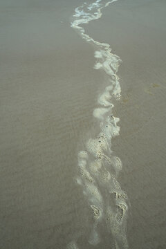 Wavy seafoam trail on wet beach sand