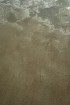 Clouds reflected on wet sand with subtle ripples and earthy tones