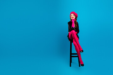 Obraz premium Chic parisian woman sits on a stool wearing pink tights and beret posing with glamour against blue background