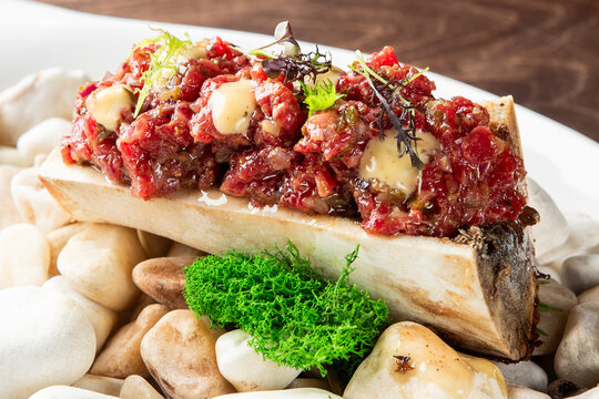 Gourmet beef tartare served in a bone marrow canoe, presented beautifully on a bed of decorative white stones with microgreens and a moss garnish