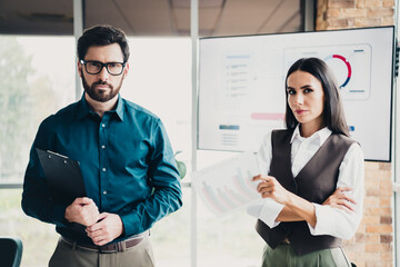 Two professionals present data in a modern office with charts on screen and a business report in...