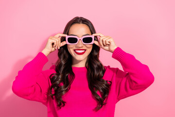 Young stylish woman wearing pink sunglasses and bright knit sweater smiles in a pink studio for fashion lifestyle imagery