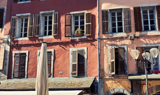 Vintage window shutters in a historic French town. Beautiful stone walls in terracotta and peach tones with open and closed wooden blinds.