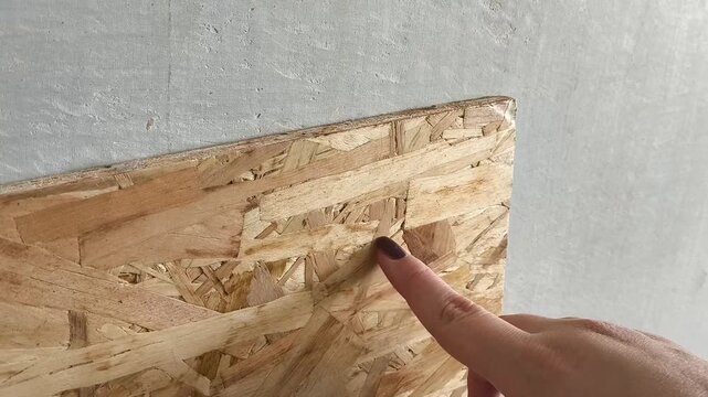 Oriented chipboard close-up. A woman's hand touches a osb wooden board made of sawdust. Building material for roughing