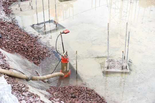Foundation dewatering, submersible pump removes groundwater from flooded excavation around concrete footings. Site drainage control, preparation for structural works.